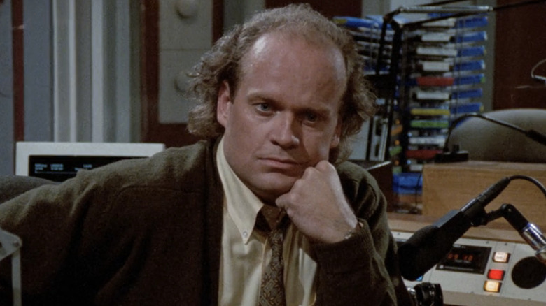 Kelsey Grammer's Frasier Crane rests his head on his fist while sitting in his radio studio in Frasier