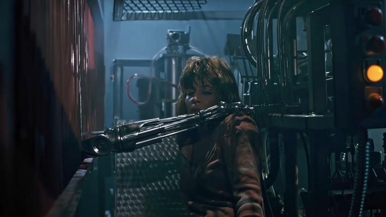 Linda Hamilton's Sarah Connor sits in a factory with the arm of the Terminator reaching for her shoulder in The Terminator