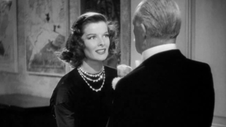 Katharine Hepburn's Linda smiles while being addressed by an older man who's facing away from camera in Holiday