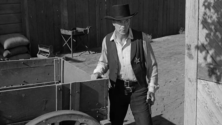 Gary Cooper stands with a gun next to a wagon in High Noon