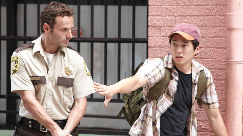 Steven Yeun as Glenn Rhee gesturing for Andrew Lincoln as Rick Grimes not to lift his gun in The Walking Dead