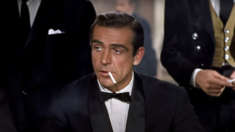 Sean Connery's James Bond sits with a cigarette in his mouth while wearing a tuxedo in Dr. No