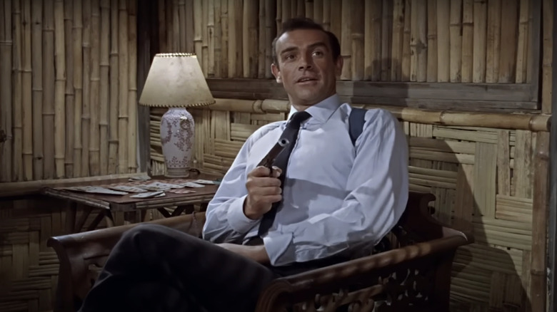 Sean Connery's James Bond sits pointing a gun at someone off screen in Dr. No