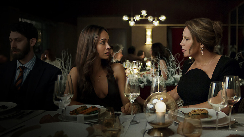 Zoe Saldana as Rita sitting at a dinner table with Karla Sofía Gascón's Emilia in Emilia Perez