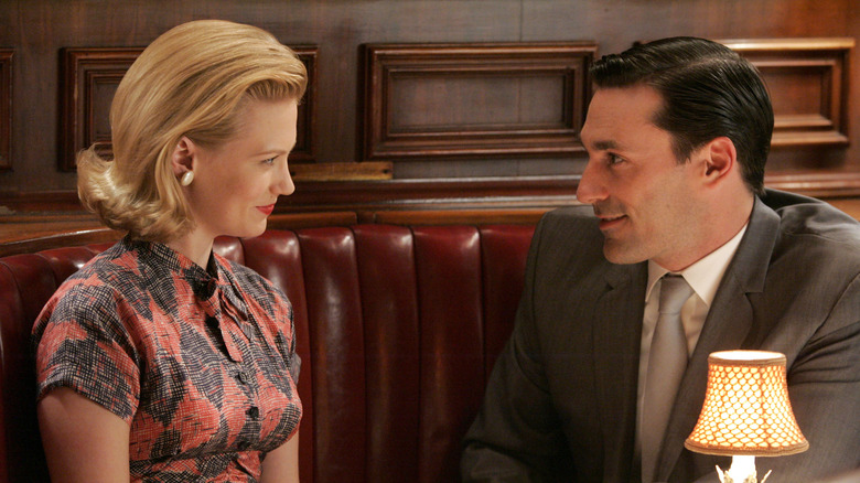 Betty Draper and Don Draper smiling at one another while sitting in a restaurant booth