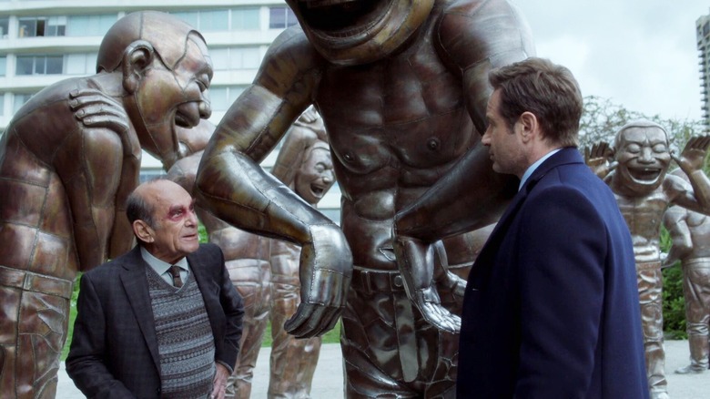 Mulder talking to the mysterious Dr. They next to some creepy laughing statues on The X-Files