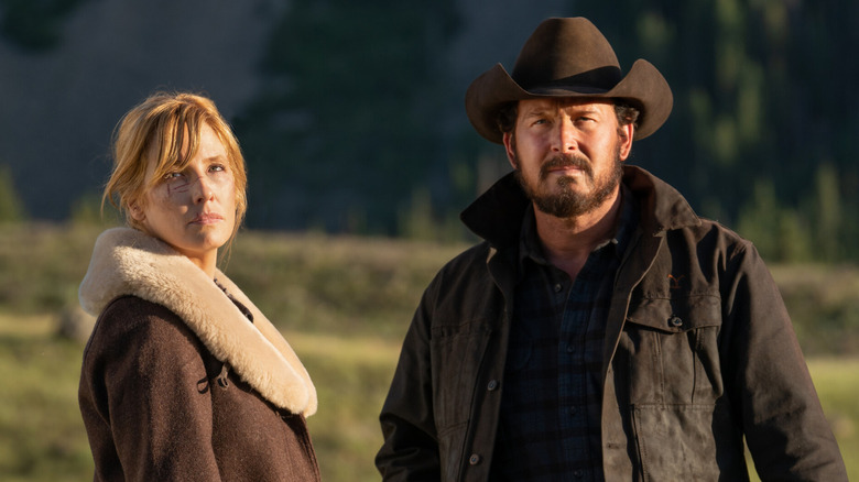 Beth and Rip standing in a field wearing coats on Yellowstone