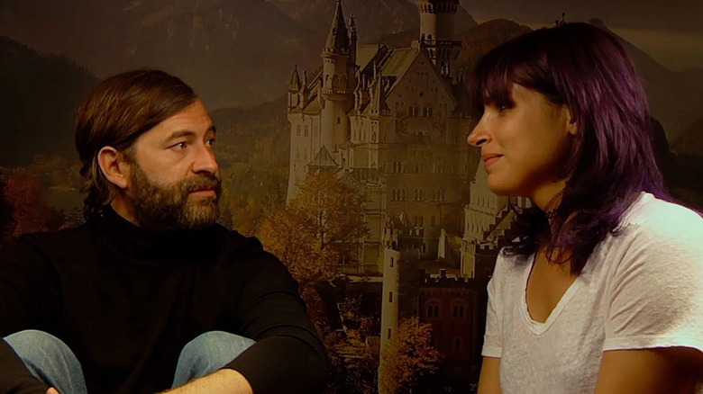 Aaron and Sar conversing in front of a photo of a castle in "Creep 2."