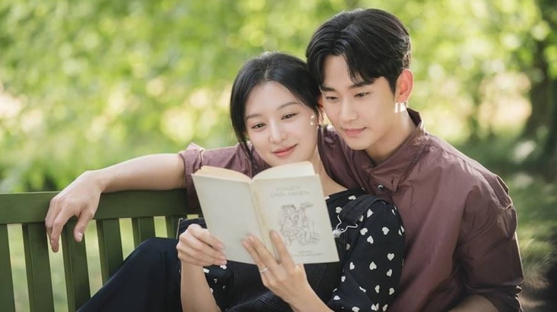 Kim Ji-won as Hong Hae-in and Kim Soo-hyun as Baek Hyun-woo read a book on a park bench in Queen of Tears