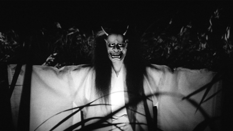 A woman wearing the han'nya mask, standing in the reeds in Onibaba