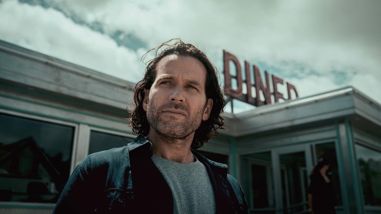 Eion Bailey as Jim standing in front of a diner in From