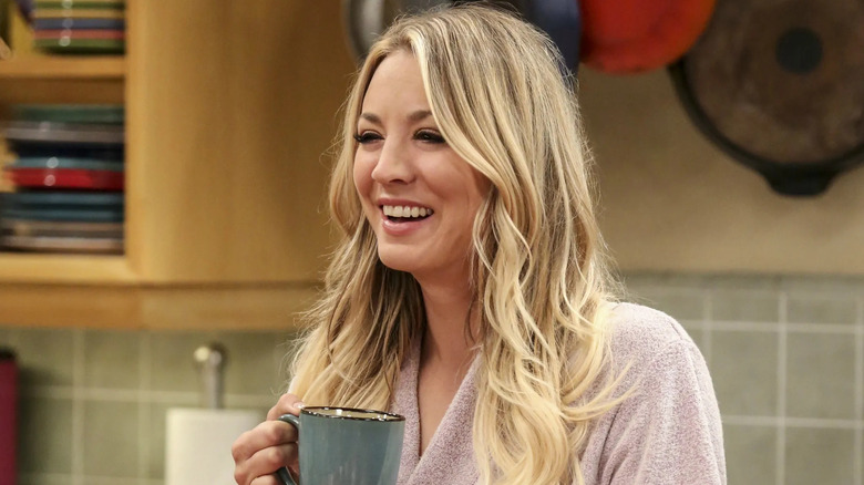 Penny holding a cup of coffee and laughing on The Big Bang Theory