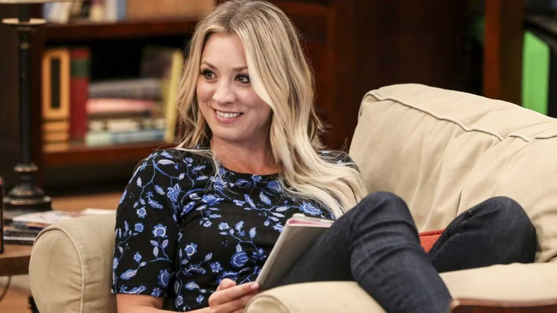 Penny está sentada en el sofá, sonriendo, en The Big Bang Theory