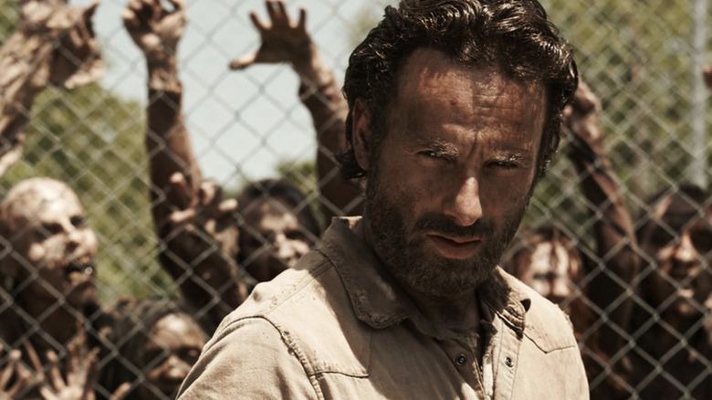 Andrew Lincoln as Rick Grimes, standing in front of a gate holding back zombies, on The Walking Dead