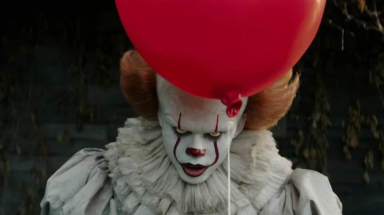 Pennywise mira amenazadoramente mientras sostiene un globo en él.