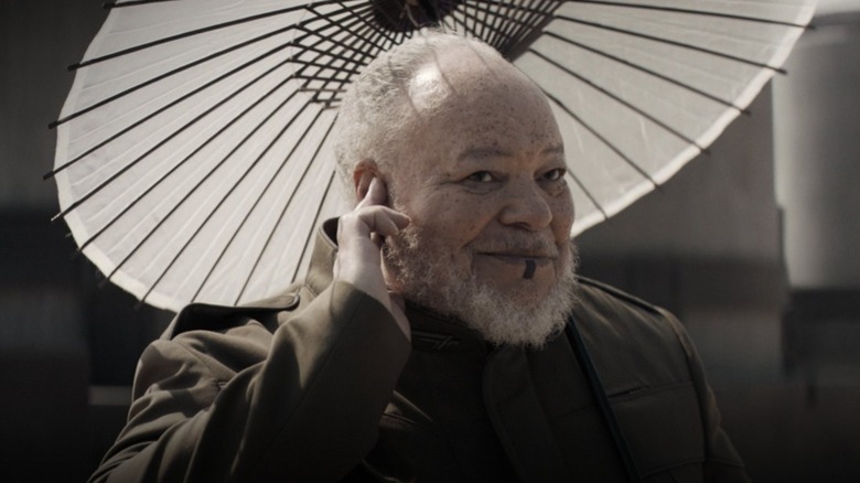 Thufir Hawat holding a cute parasol and checking his ear piece in Dune