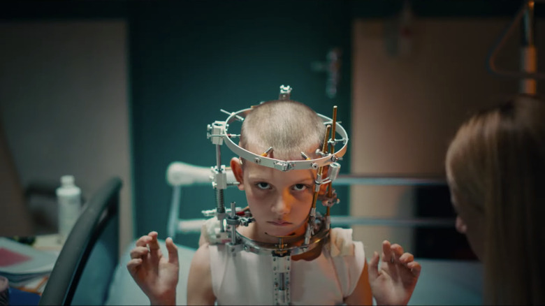 child with metal headbrace sitting down with her arms up