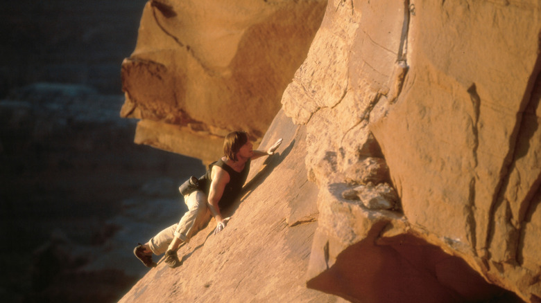 Ethan Hunt, with long hair, climbing up a rock face at the beginning of 