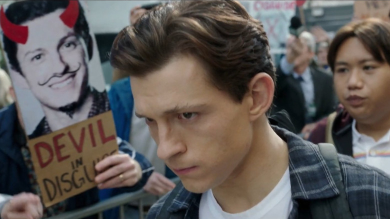 Tom Holland as Peter Parker walking by a protest sign calling him the devil in disguise in Spider-Man: No Way Home