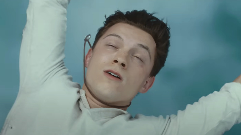 Tom Holland's Nathan Drake closes his eyes as he's swept by a strong wind in Uncharted