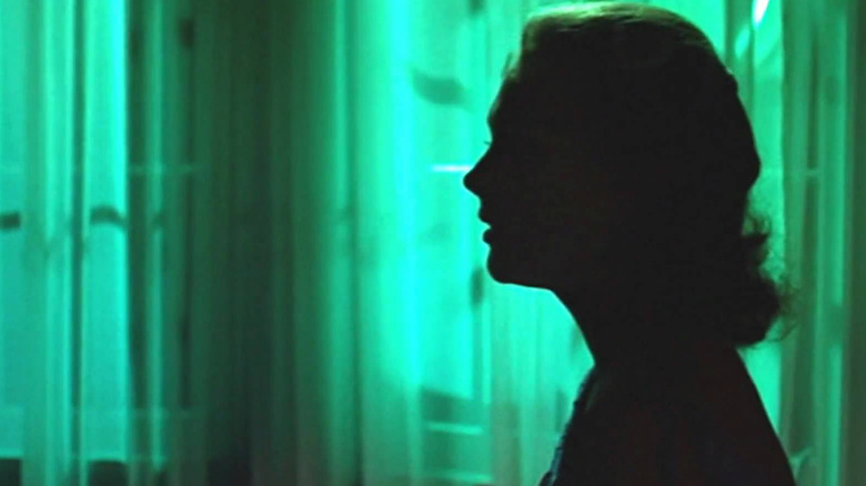 Kim Novak stands in profile, bathed in green light
