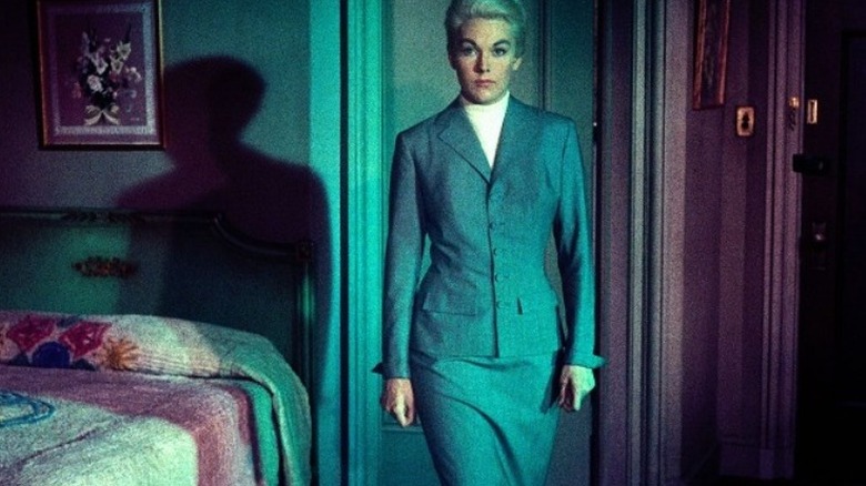 Kim Novak stands in a grey suit 