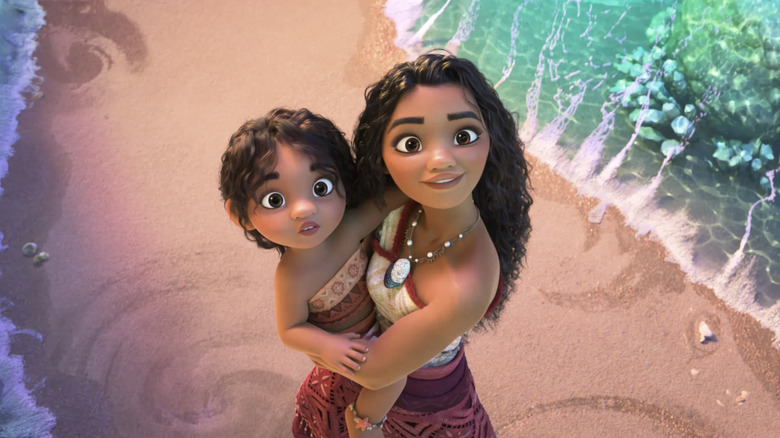 Moana holding her little sister Simea as they look up at the ocean waves in Moana 2