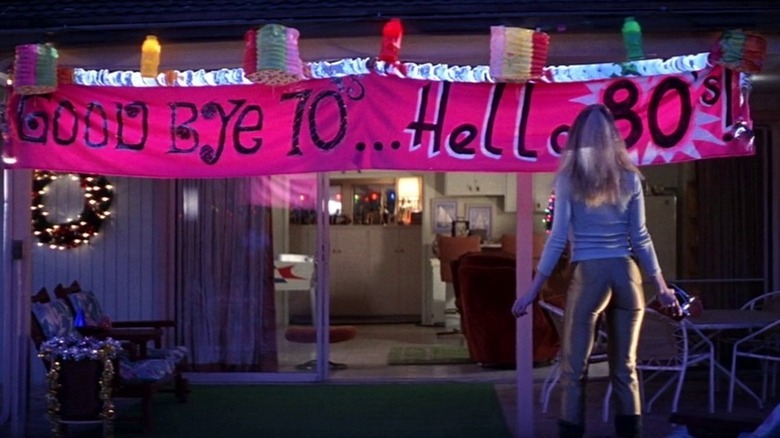 Heather Graham in Boogie Nights, standing next to a banner that says "Goodbye 70's... Hello 80's"