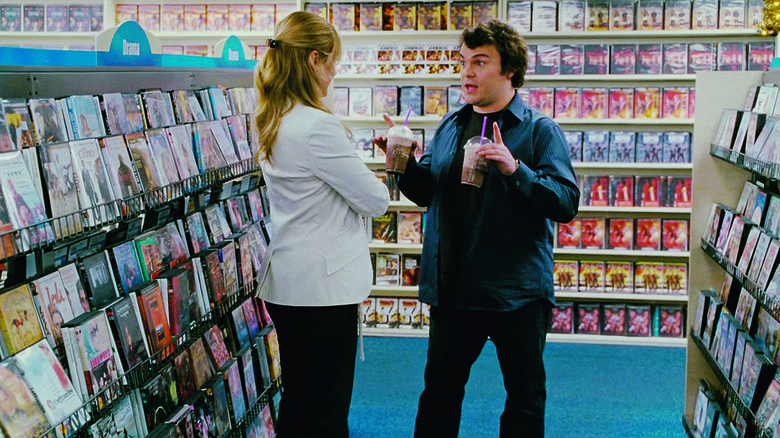 Miles talking to a woman in a video store, he has two fancy coffee drinks in his hands. From The Holiday.