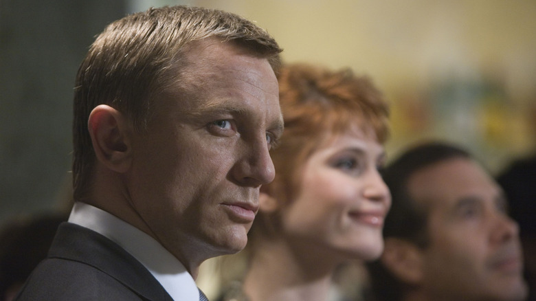 James Bond in a suit sitting next to well-dressed people, looking suspicious