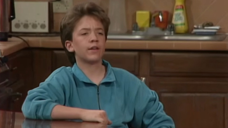 David Faustino as Bud Bundy sitting at a table and speaking on Married with Children