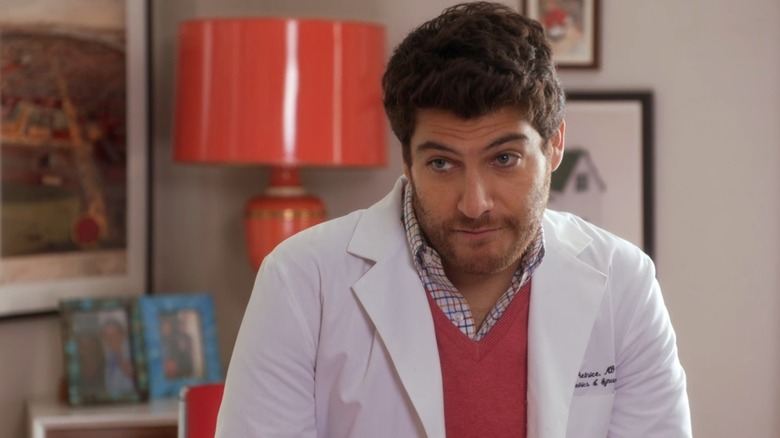 Dr. Peter Prentice (Adam Pally) looking skeptical in his lab coat over a pink v-neck sweater, on The Mindy Project