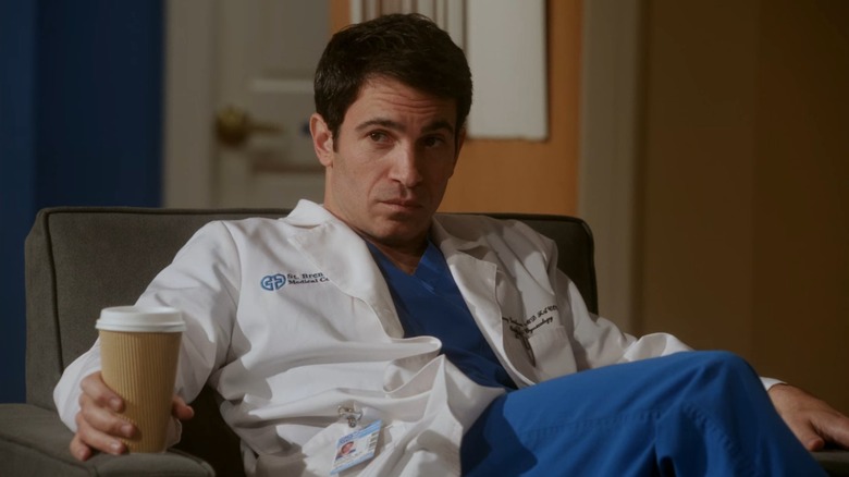 Dr. Danny Castellano (Chris Messina) in his lab coat, reclining in a chair holding a coffee cup, on The Mindy Project