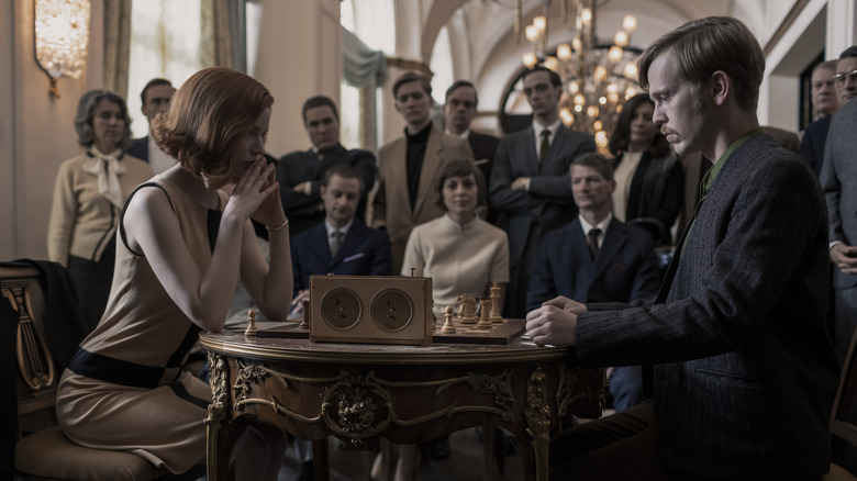 Beth Harmon playing chess in a tournament while onlookers watch in The Queen's Gambit