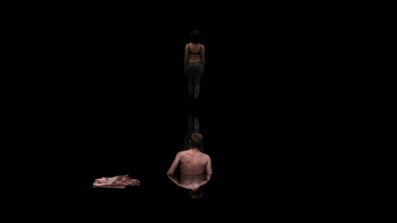 Shirtless Laura walking ahead of man sinking into blackness in Under the Skin