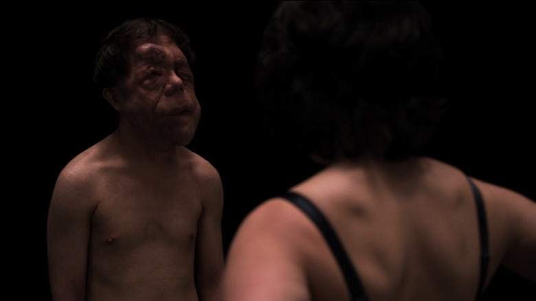 Laura in bra standing in front of shirtless man with facial deformity in Under the Skin