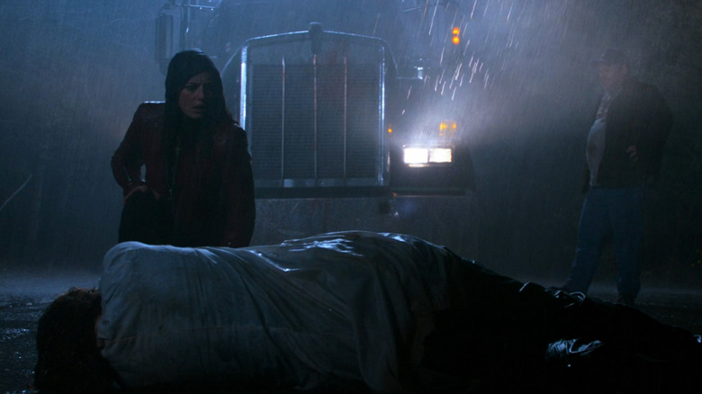 trucker and woman standing on rainy road near a body