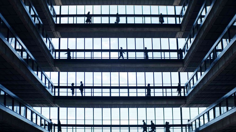 The inside of Lumon headquarters, a large, multi-floor window in front. People walk along walkways.