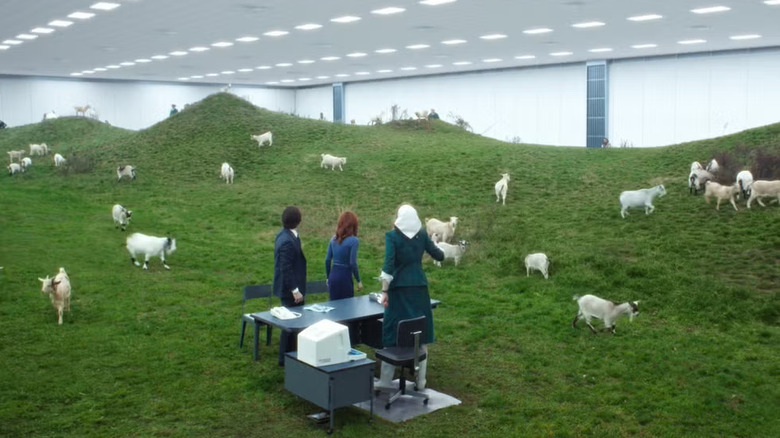 The Goat Room, a grassy, hilly place enclosed by a massive office ceiling. There is a desk on the grass, and goats everywhere. A scene from Severance.