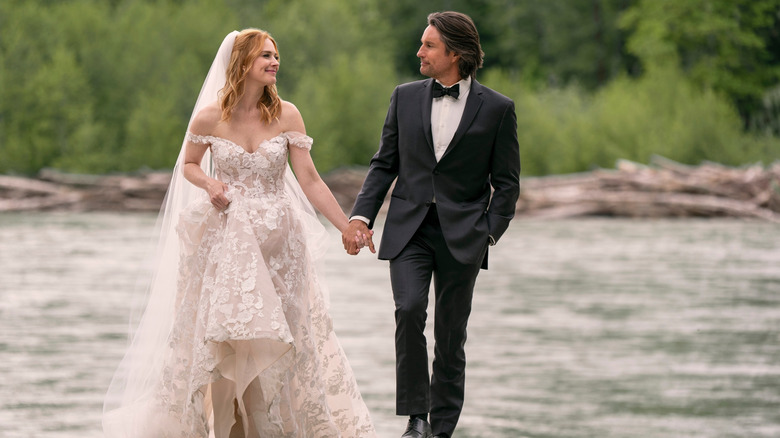 Mel Monroe (Alexandra Breckenridge) and Jack Sheridan (Martin Henderson) walk hand in hand, she dressed in a bridal gown and he in a tuxedo, in "Virgin River"