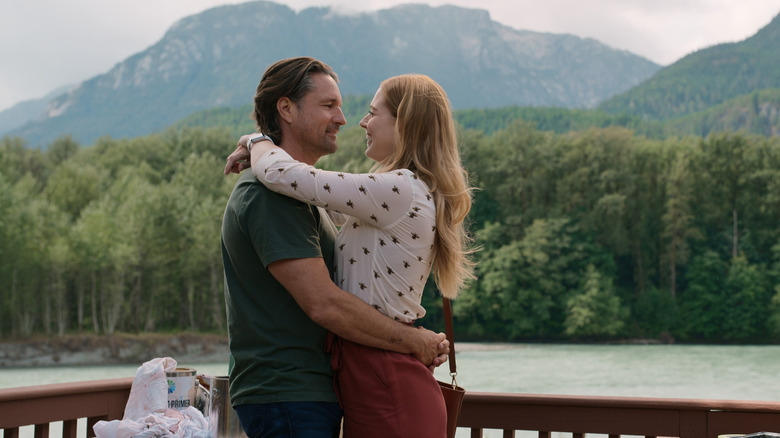 Jack Sheridan (Martin Henderson) e Mel Monroe (Alexandra Breckenridge) se mantêm e sorriam contra um cenário montanhoso em 