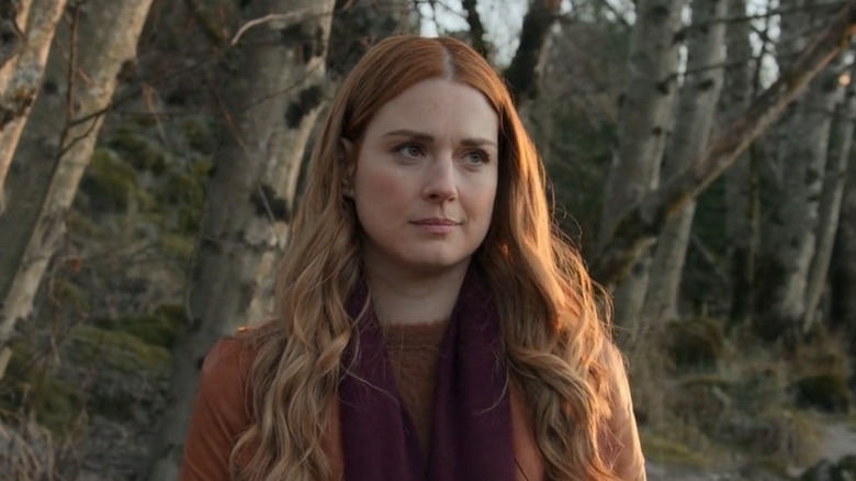 Mel Monroe (Alexandra Breckenridge) stands outside a forested area and looks off to her left