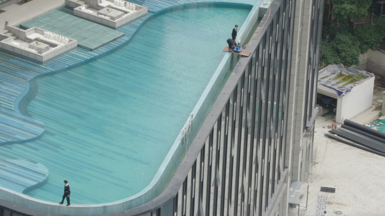 three people walking on the roof ledge of a building next to a rooftop pool