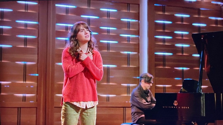 a woman with her arms crossed against her chest while performing on stage next to a pianist