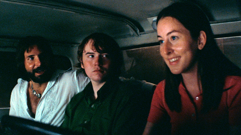 a man and a younger boy look at a smiling girl behind the wheel