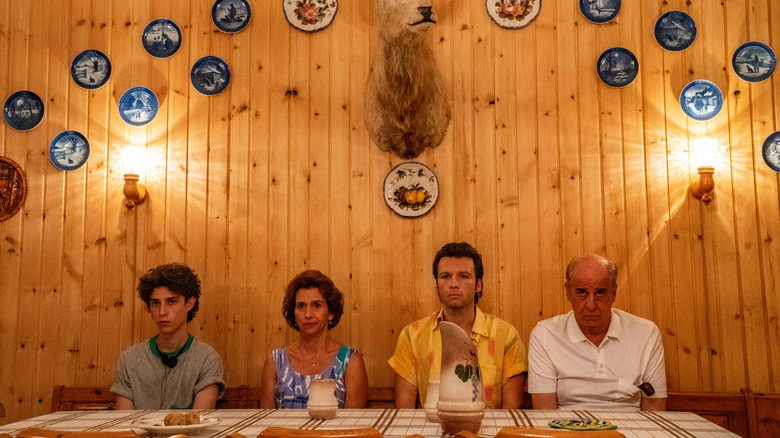 three men and one woman sitting at a table in front of a wood wall with plates and a deer head