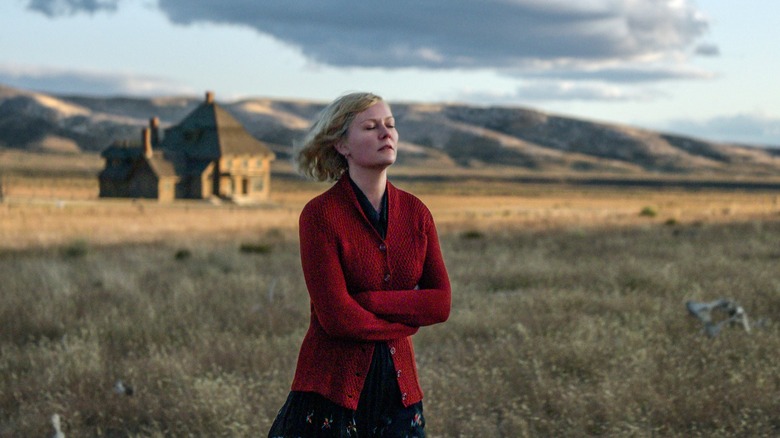 a woman in a red sweater with her eyes closed in a field with a house in the background