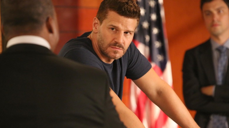 David Boreanaz's Seeley Booth leans over in a t-shirt with an American flag in the background on Bones