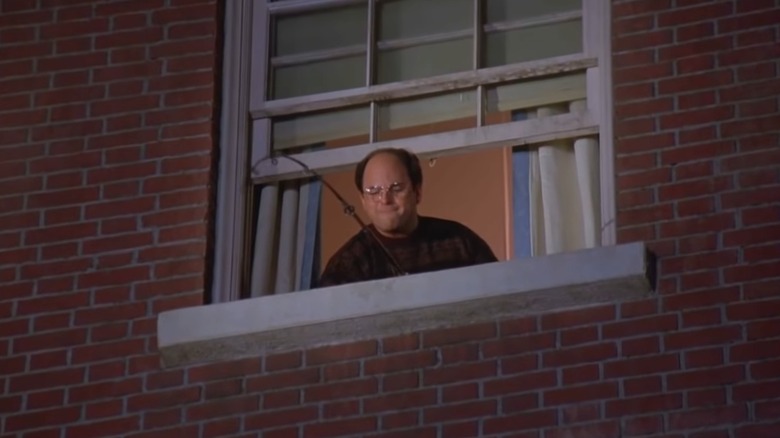 Jason Alexander's George reels in a fishing pole from the window of a brick building in Seinfeld