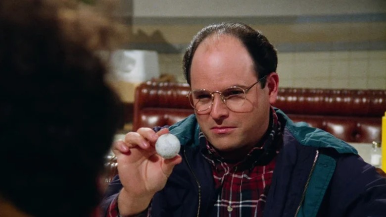 Jason Alexander's George holds up a ping pong ball in the diner in Seinfeld